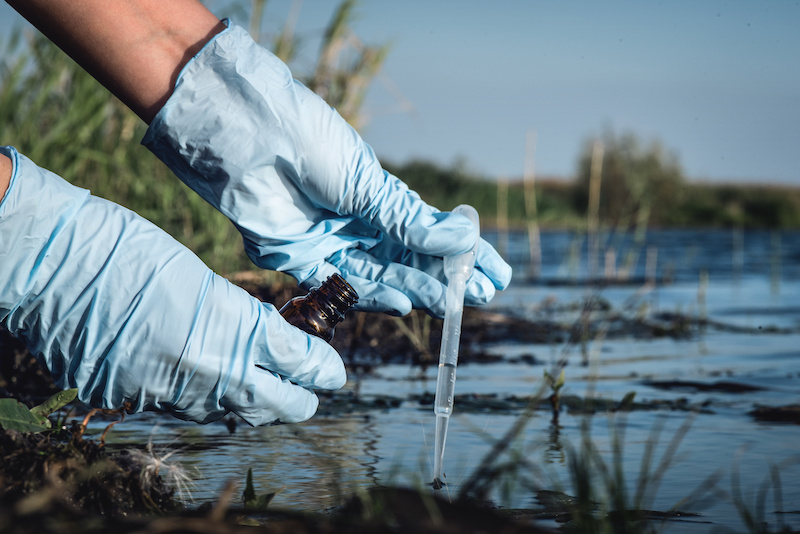 Donna coni guanti preleva un campione d'acqua con una pipetta da un fiume o un lago; concept: inquinamento delle acque