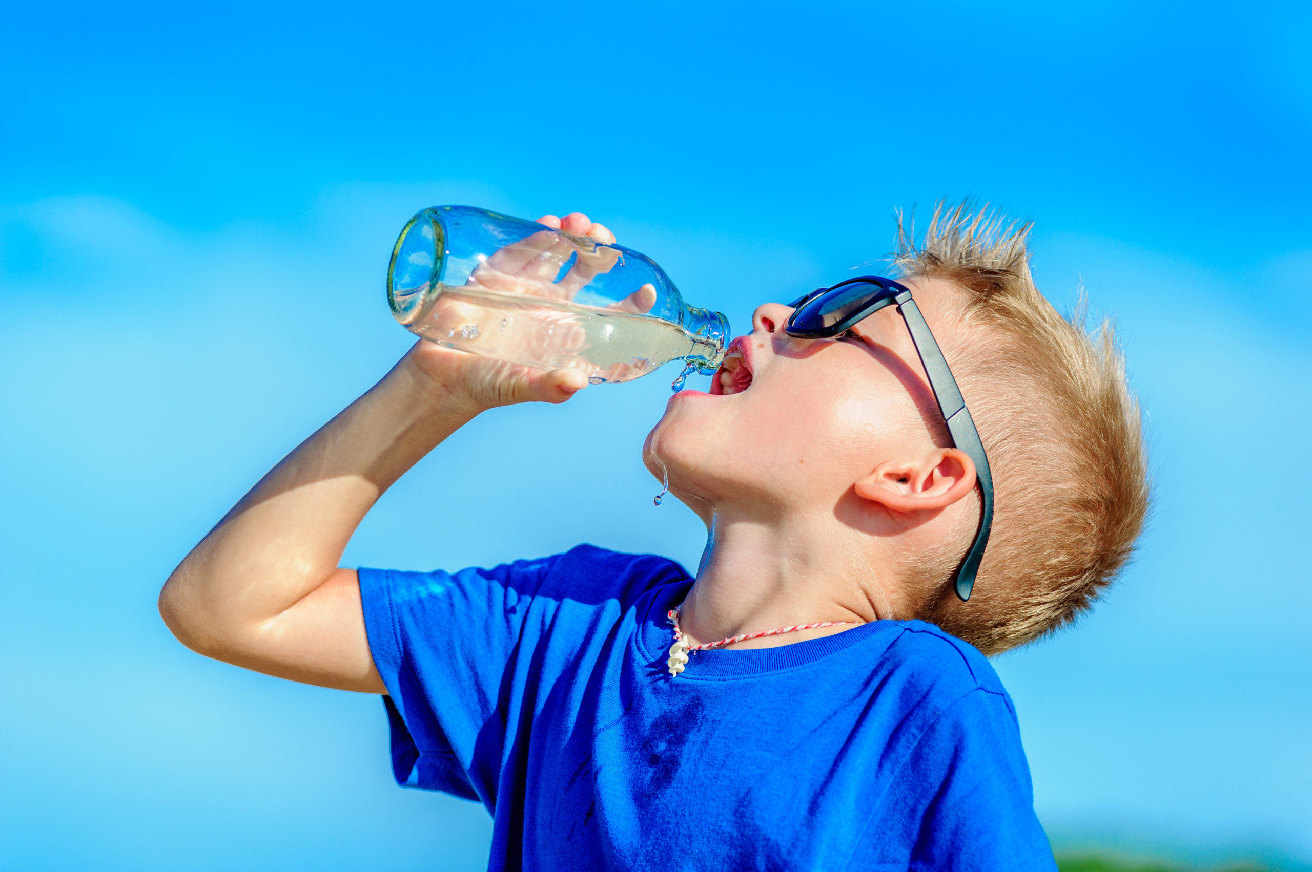 Portrait of a thirsty handsome boy in sunglasses drinking water on the desert tropical beach