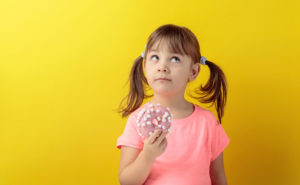 Bambina pensierosa con una ciambella glassata o donut in mano; concept: bambini, dolci, merendine