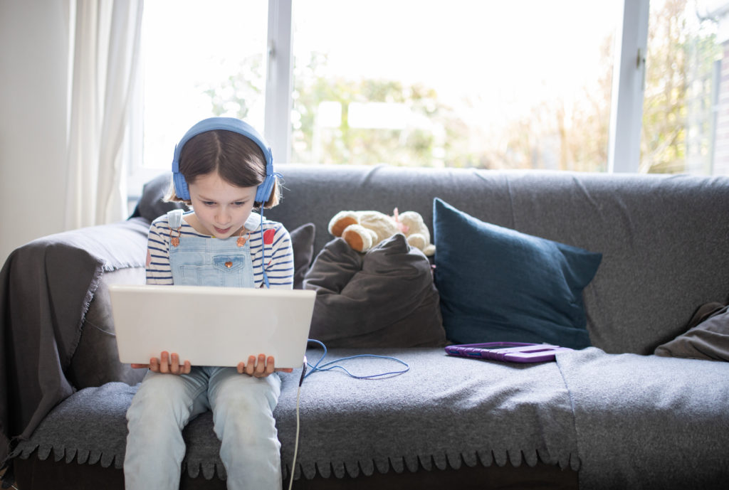 female child sitting on the sofa at home with a laptop and head phones