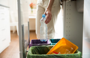 spazzatura riciclo riciclaggio packaging confezioni Woman putting empty plastic bottle in recycling bin in the kitchen. Person in the house kitchen separating waste. Different trash can with colorful garbage bags.