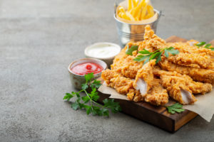 Stirps o nuggets di pollo panato e fritto con erbe aromatiche, ciotoline di ketchup e maionese e sullo sfondo patatine fritte