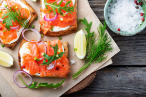 tartina salmone affumicato su tagliere con erbe aromatiche, lime e cipolla e ciotola di sale grosso