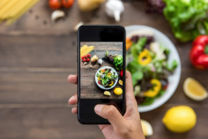 Food blogger che fotografa con lo smartphone una bella insalata, spaghetti crudi e ingredienti su un tavolo di legno per condividerli sui social media vegan vegano vegetariano