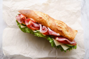 Baguette con prosciutto, formaggio, insalata, pomodori e cetrioli su carta da forno; concept: panino