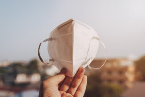 The Hand holding the mask (KN95 or N95 mask for protection pm 2.5 and coronavirus, COVID-19) up in the sky. Virus spread around the world. pandemic virus. Hope for vaccine or treatment concept.