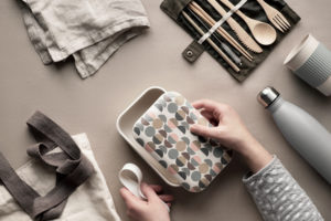 Kit per il pranzo al sacco a rifiuti zero nelle mani. Set per il pranzo da asporto - sacchetto di cotone, organizer di posate in bambù, lunch box in bambù e tazza riutilizzabile. Stile di vita sostenibile, vista dall'alto su carta artigianale. bambu plastica