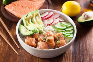 ciotola di poke con salmone avocado cetriolo ravanello con bacchette, trancio di slamone e limone sullo sfondo