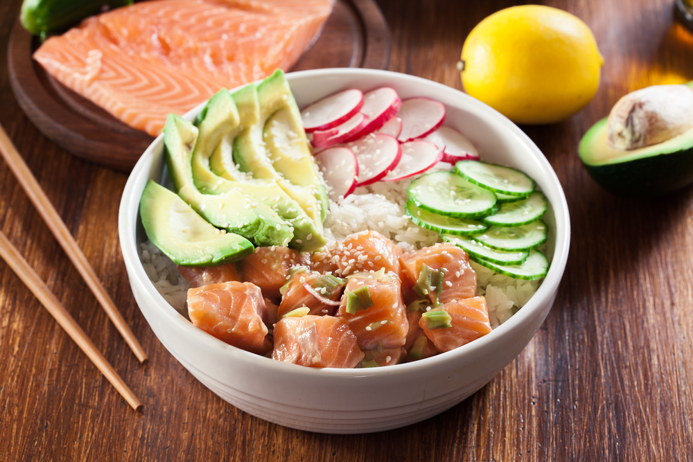 ciotola di poke con salmone avocado cetriolo ravanello con bacchette, trancio di slamone e limone sullo sfondo