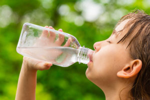 Una bambina beve acqua da una bottiglietta; concept: minerale, acqua del rubinetto