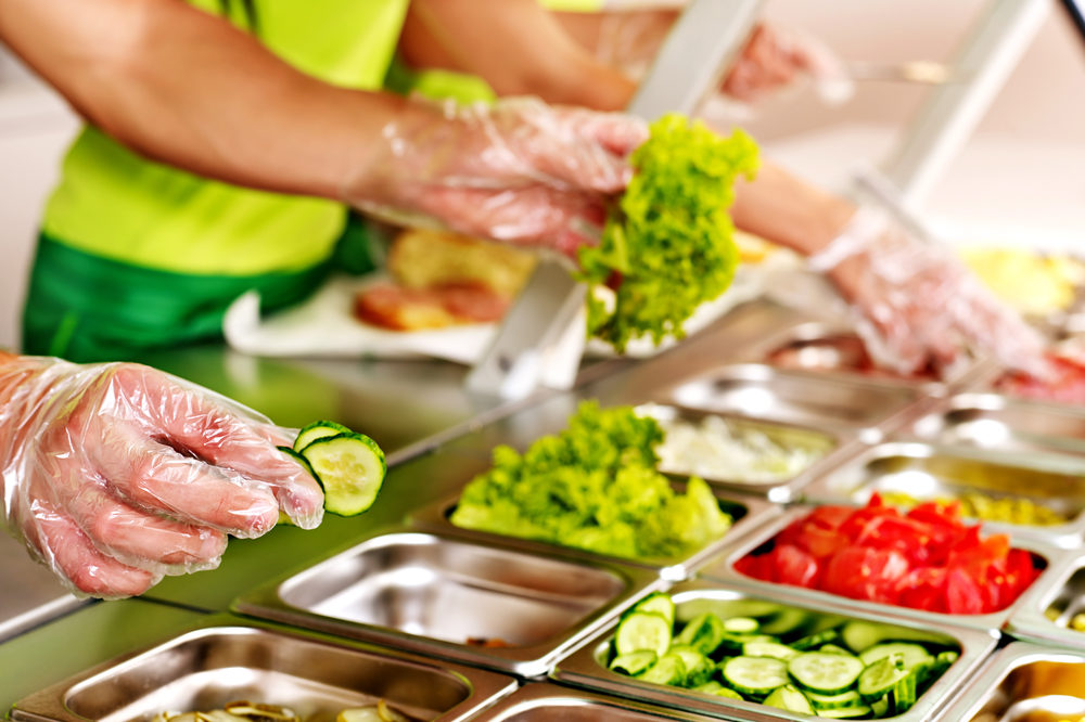 Operatrici prendono cibo da pozzetti da un bancone di una mensa scolastica o lavorativa