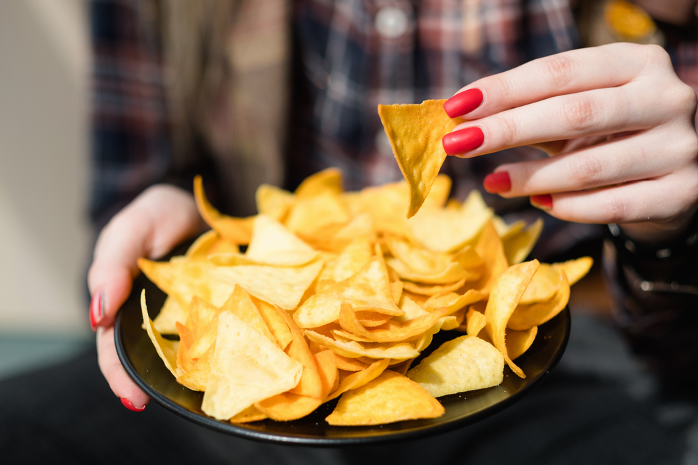 Donna prende tortilla chips da un piattino; concept: junk food, ultra processati, snack