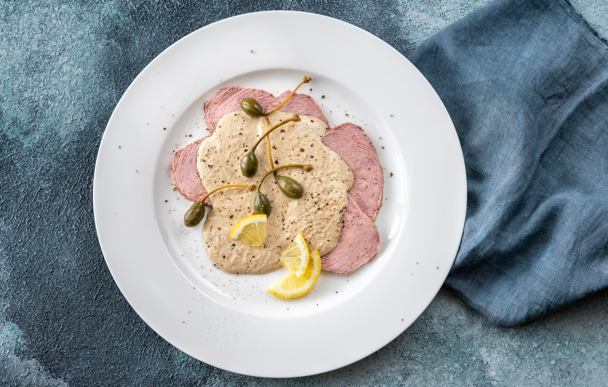 Piatto di vitello tonnato o vitel tonnè con frutti dei capperi (cucunci), fette di limone e pepe