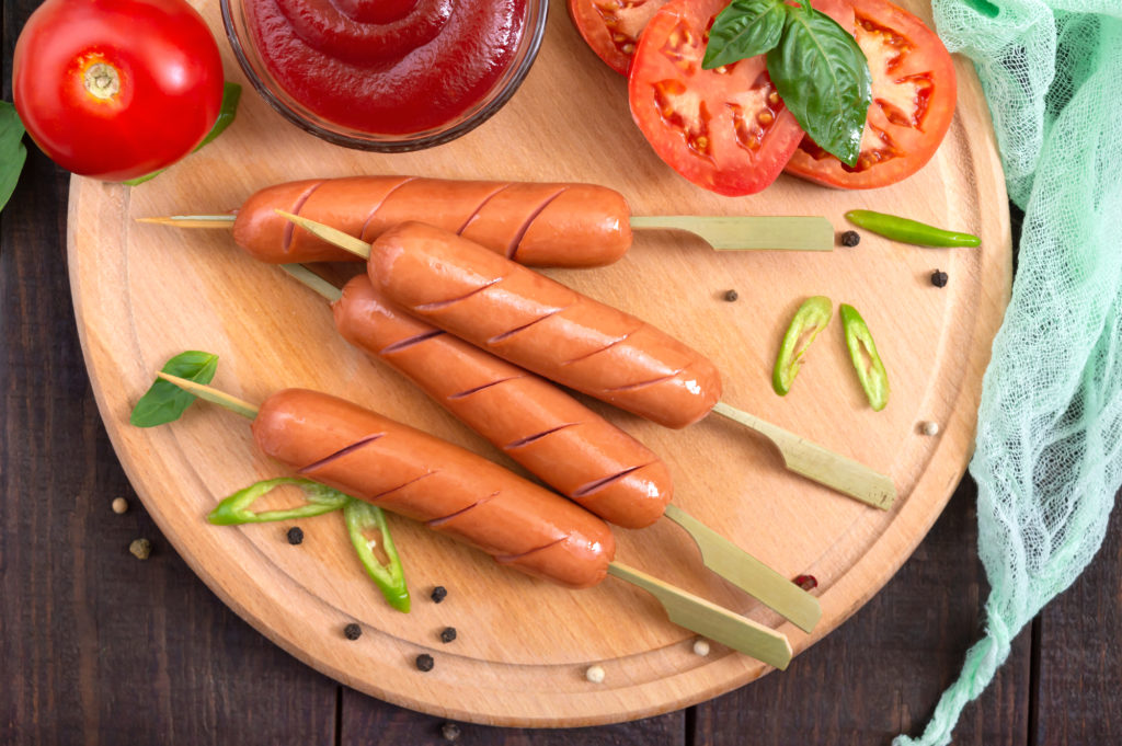 Wurstel su spiedini di legno su un piatto di legno con fette di pomodoro, e salsa