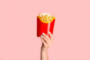Mano femminile con smalto bianco che mostra patatine fritte da McDonald's in confezione rossa su sfondo rosa