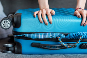 mani di donna con smalto marrone che tenta di chiudere valigia azzurra