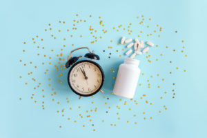 Sveglia analogica e flaconcino con compresse di integratore alimentare su una superficie azzurra con stelline dorate