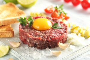 Tartare di manzo con tuorlo d'uovo su un tavolo di legno blu