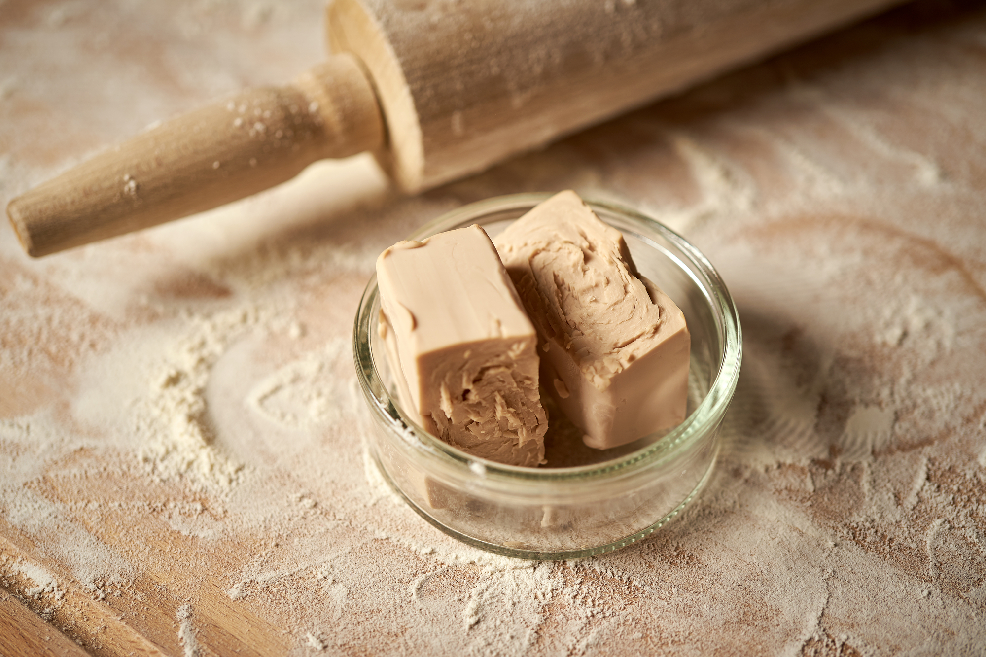 Primo piano di lievito fresco in una ciotola di vetro su un tavolo di legno bianco.