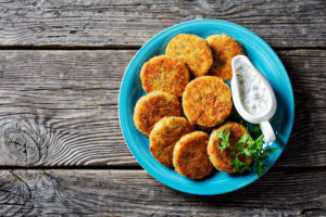 Polpette facili di filetto di pesce bianco: merluzzo o eglefino con patate e prezzemolo, impanato nel pangrattato servito su un piatto con salsa tartara in una salsiera su fondo di legno, vista dall'alto, primo piano vegetariano vegan vegano vegetariano vegetale