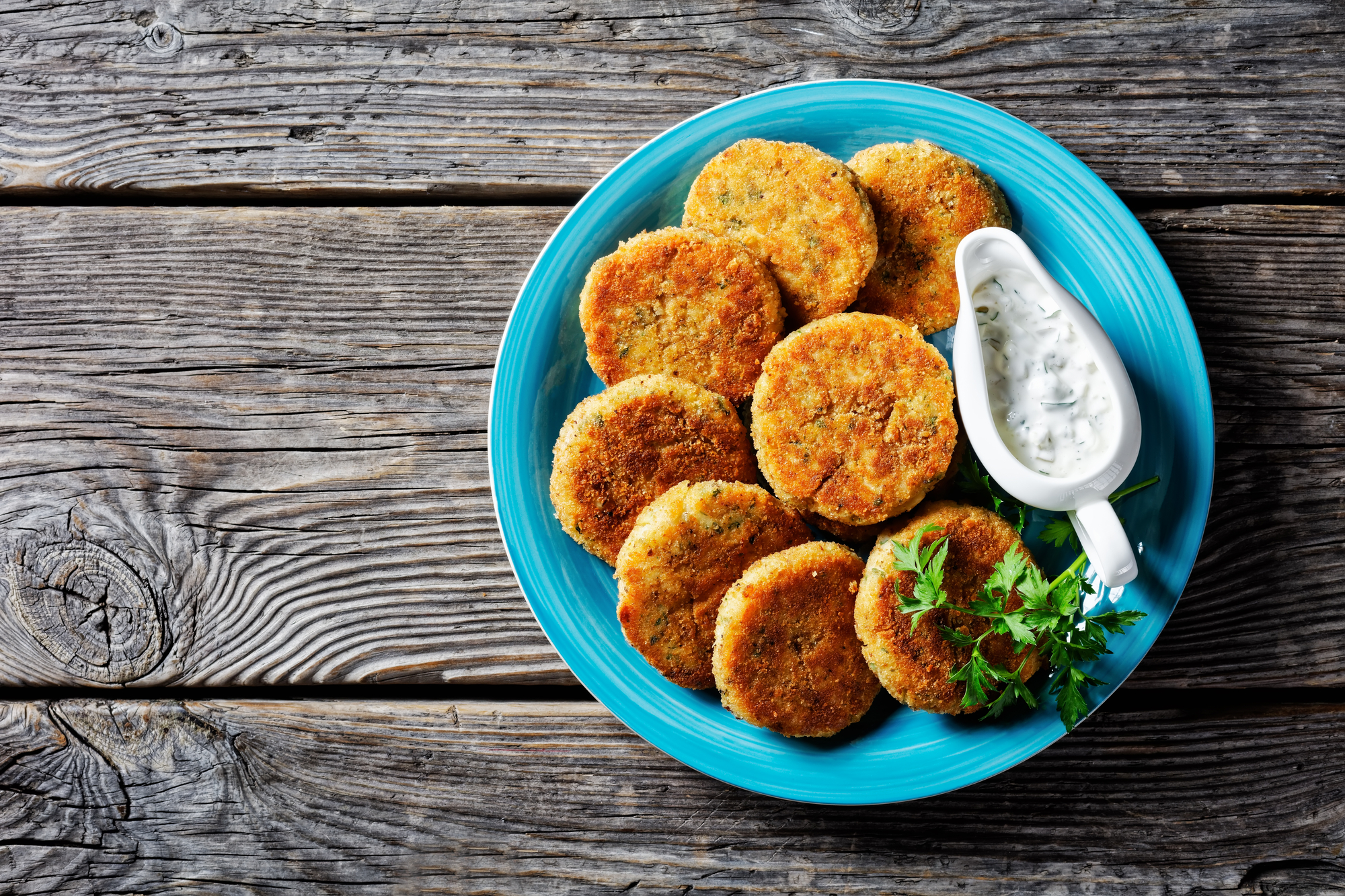 Polpette facili di filetto di pesce bianco: merluzzo o eglefino con patate e prezzemolo, impanato nel pangrattato servito su un piatto con salsa tartara in una salsiera su fondo di legno, vista dall'alto, primo piano vegetariano vegan vegano vegetariano vegetale