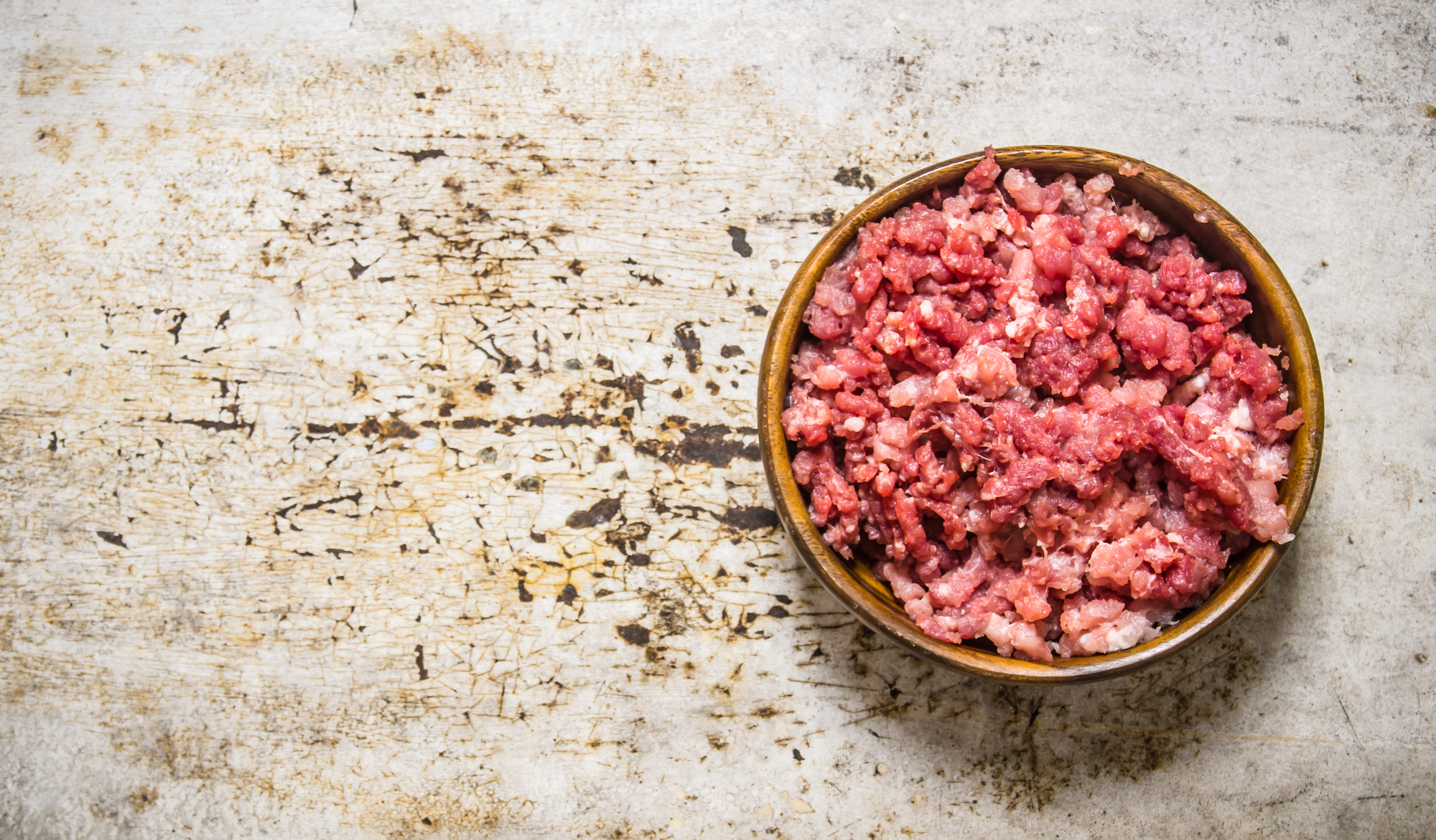 Carne macinata cruda fresca in una ciotola di legno. Su fondo rustico. macinato barf