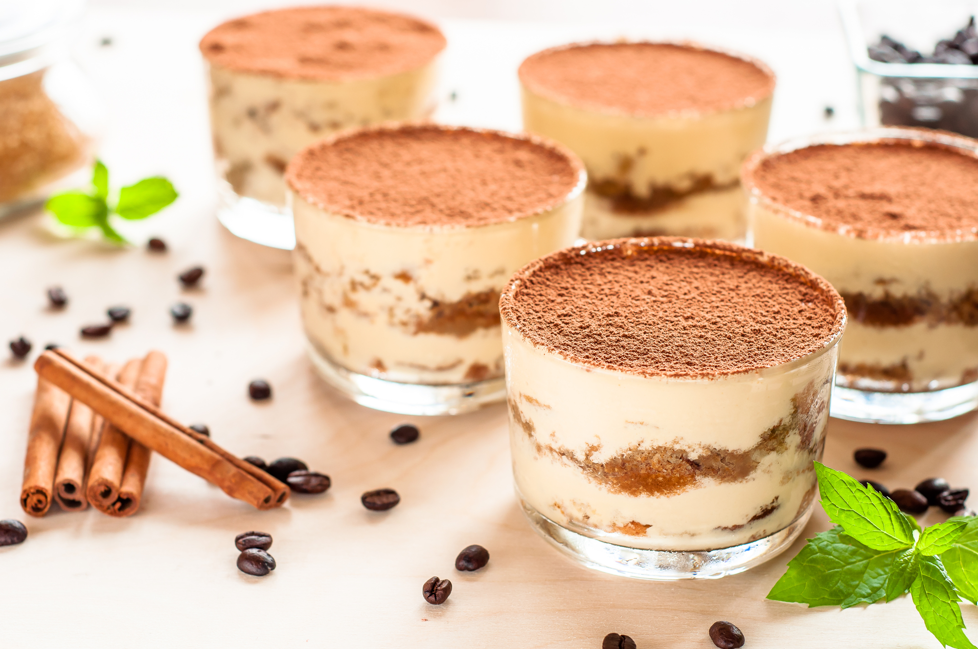 Tiramisù in bicchieri di vetro, circondati da chicchi di caffè, stecche di cannella e foglie di menta
