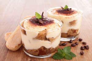 Tiramisu in bicchieri di vetro con savoiardi, chicchi di caffè e foglie di menta