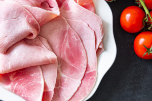 Prosciutto cotto affettato su un piatto accanto a pomodorini a grappolo; concept: nitriti