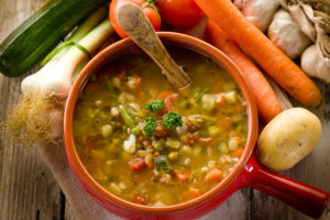 Minestrone di verdura in pentola di coccio, circondata da verdure
