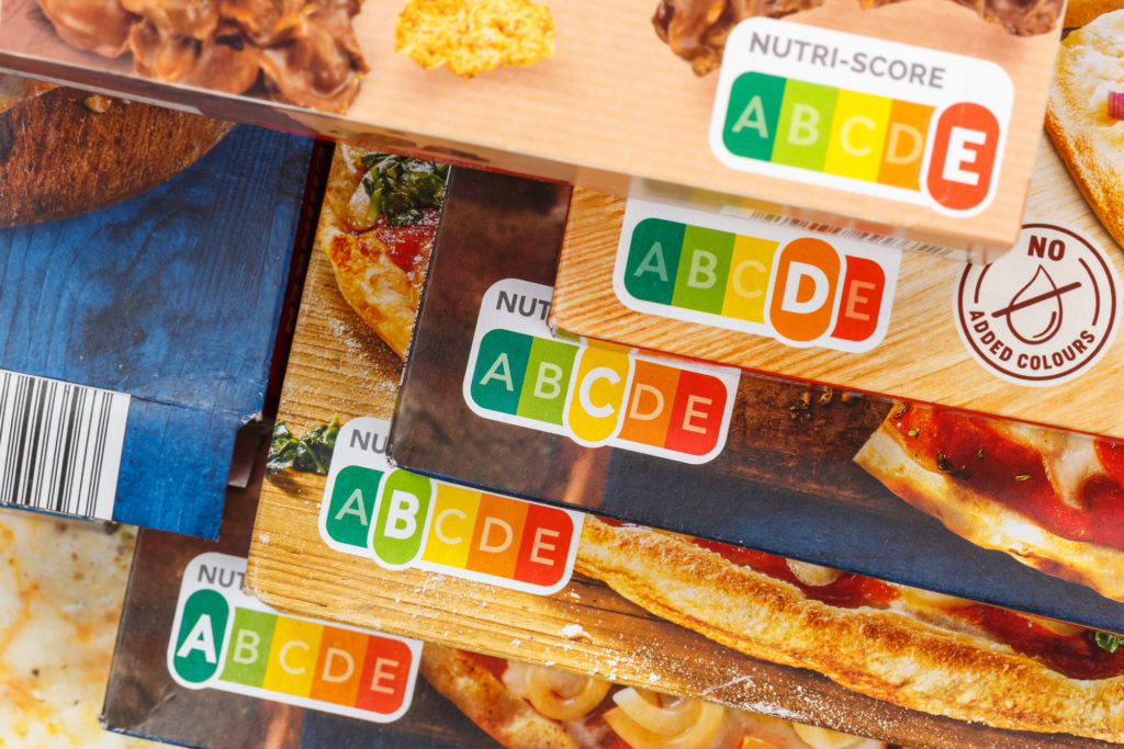 Nutri-Score da A ad E su diverse confezioni di pizza surgelata sovrapposte in scala