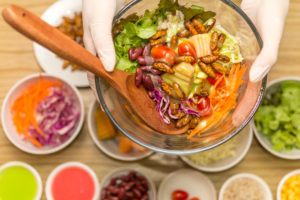 Mani con guanti tengono un'insalatiera di vetro con insalata di verdure e larve di insetti sopra tante ciotole di vetro con gli ingredienti