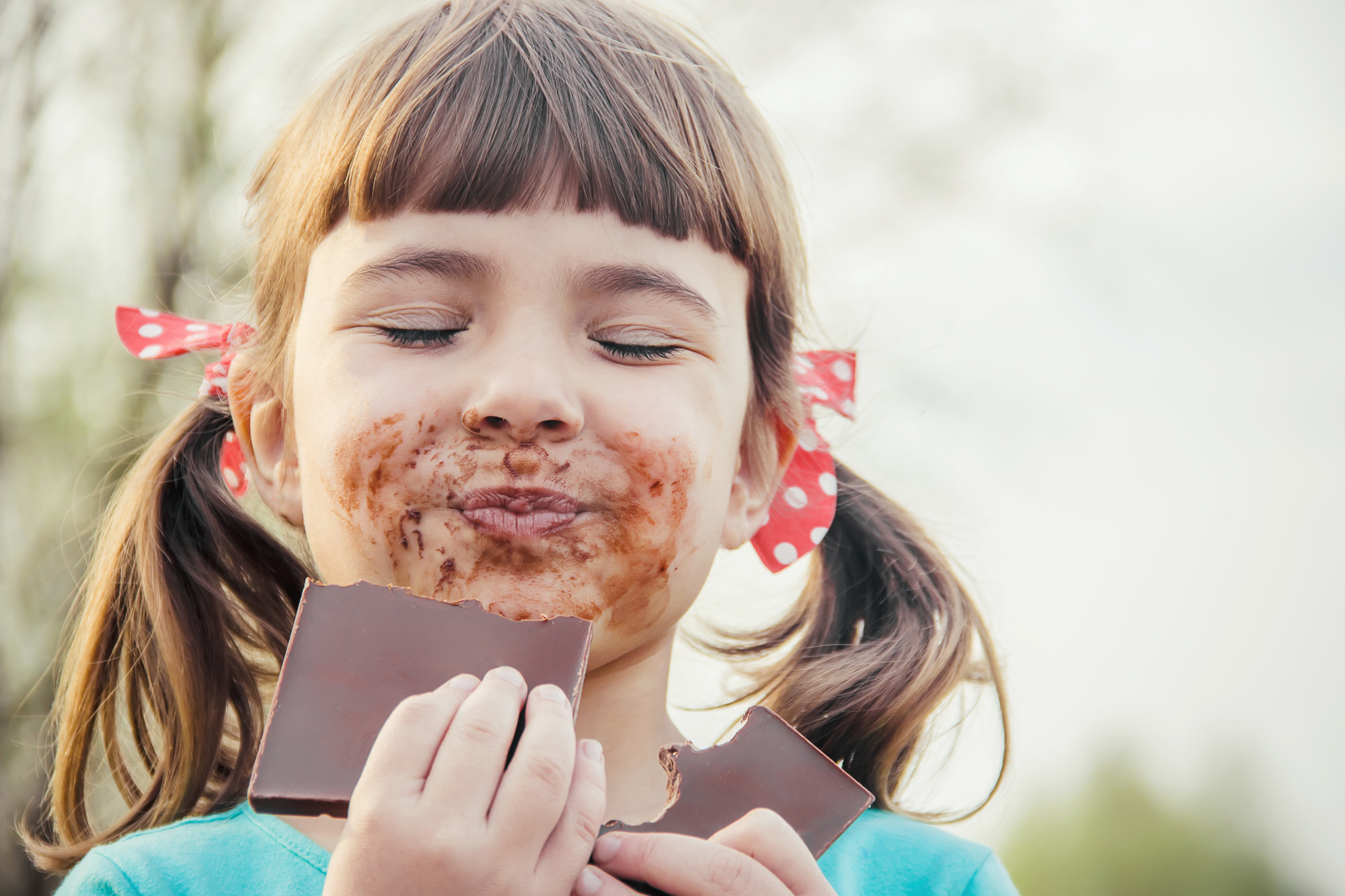 Bambina con faccia sporca di cioccolato mangia una tavoletta di cioccolato bambini
