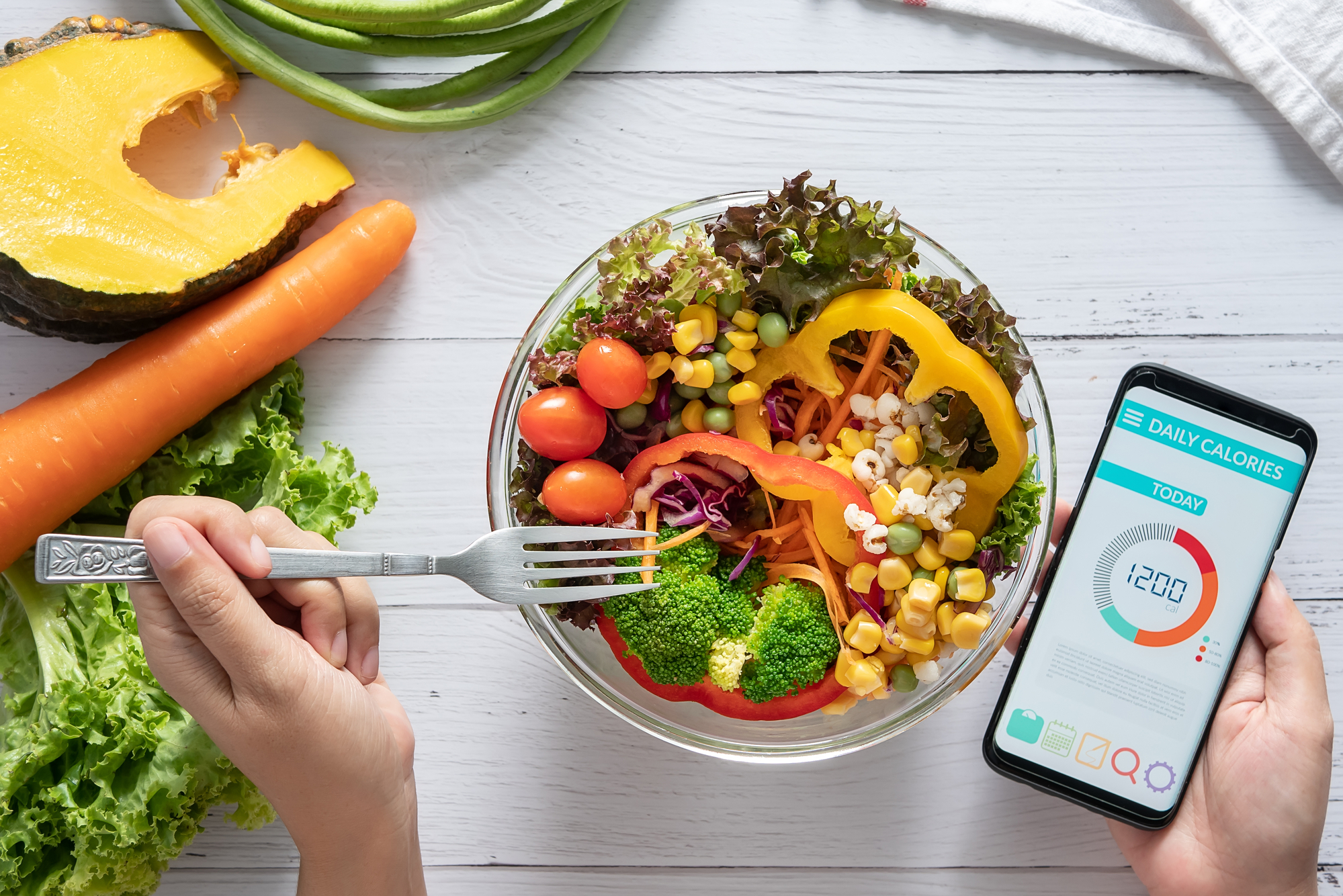 Una persona mangia un'insalata di cereali, verdure e legumi, mentre tiene in mano uno smartphone con app conta calorie; concept: dieta