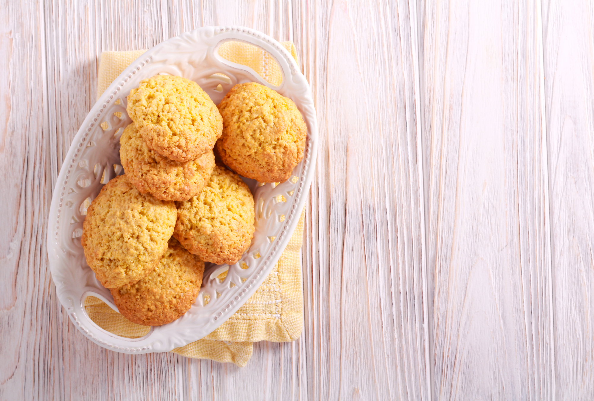 Biscotti di mais in un cestino bianco su un tovagliolo ripiegato su tavolo di legno chiaro