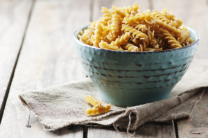 Pasta integrale tipo fusilli in una ciotola azzurra, su una tovaglietta grezza