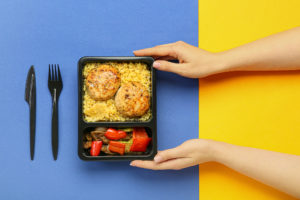 Donna tiene tra le mani cibo in un contenitore in plastica per asporto, takeaway o food delivery, con posate di plastica