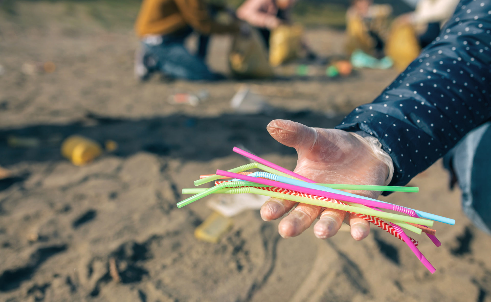 Donna con guanto mostra cannucce di plastica raccolte tra i rifiuti su una spiaggia