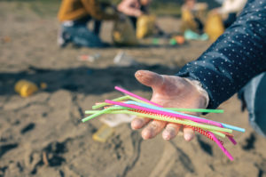 Donna con guanto mostra cannucce di plastica raccolte tra i rifiuti su una spiaggia