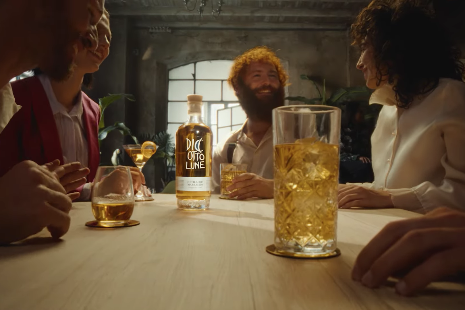 Grappa 18 Lune spot: un gruppo di persone attorno a un tavolo con al centro la bottiglia e bicchieri di diverse dimensioni