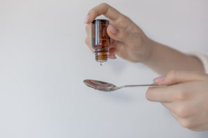 Donna fa cadere gocce di farmaco o integratore su un cucchiaino da un flaconcino; concept: integratori alimentari, farmaci