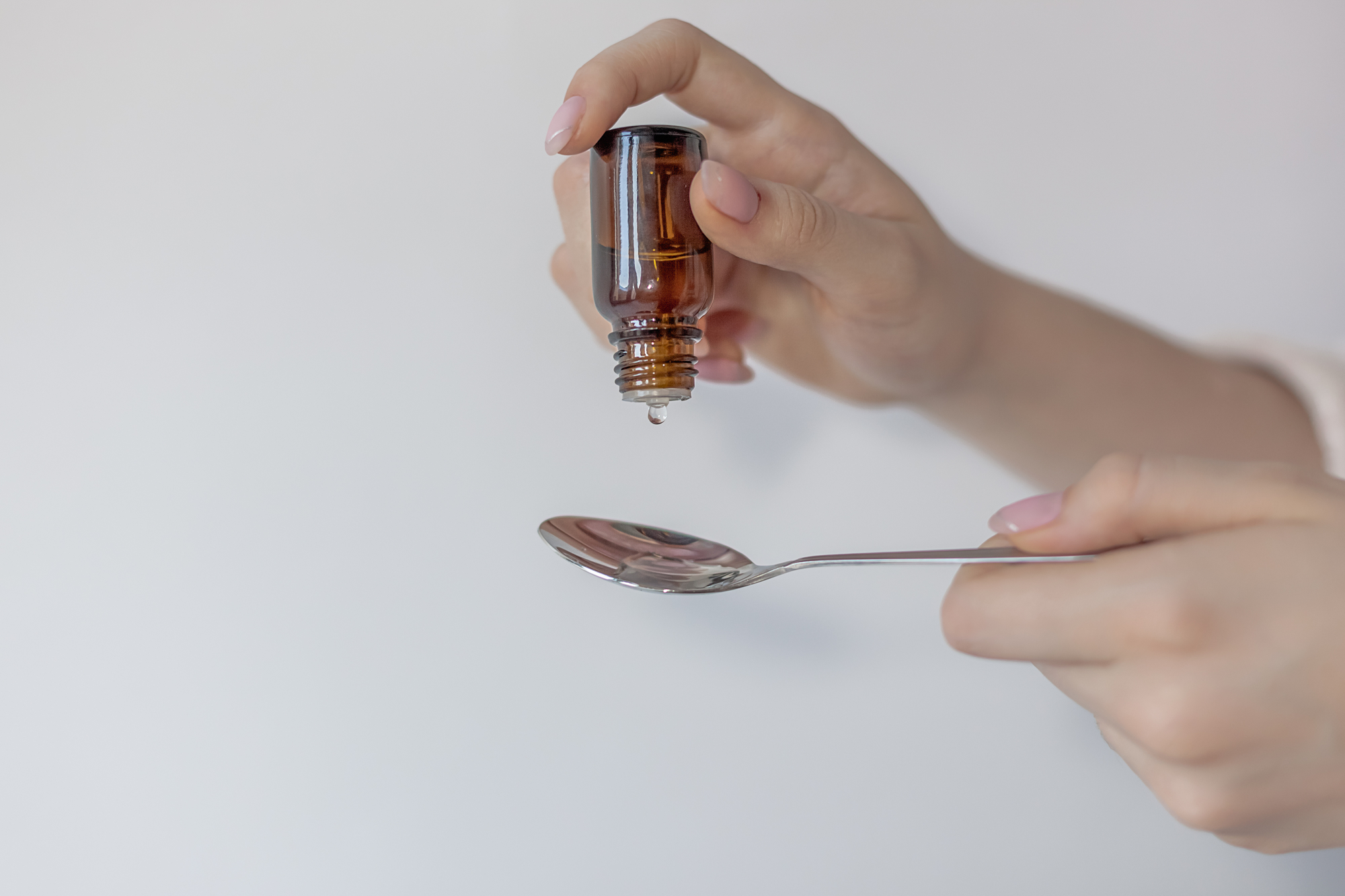 Donna fa cadere gocce di farmaco o integratore su un cucchiaino da un flaconcino; concept: integratori alimentari, farmaci