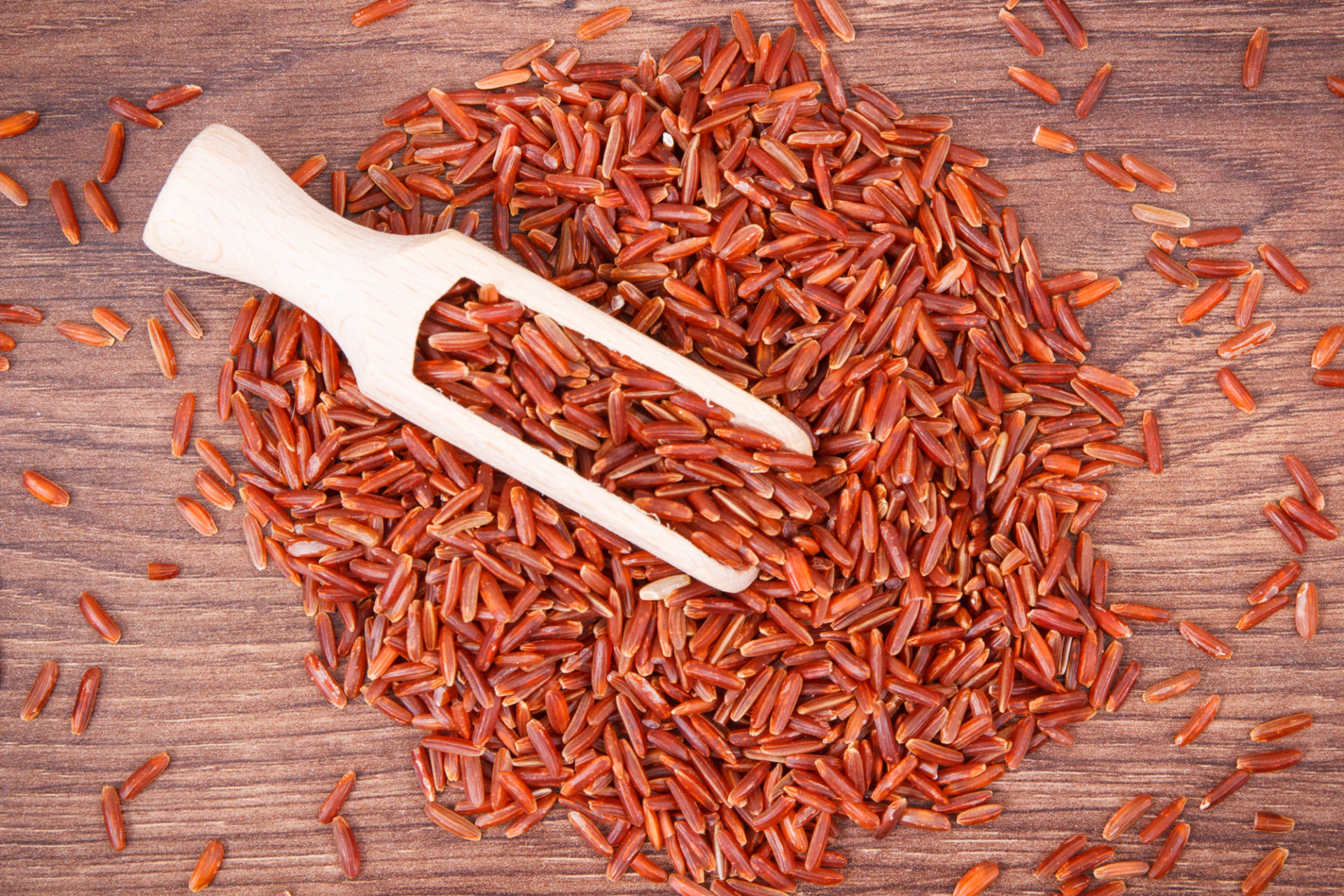 Riso rosso sparso su un tavolo di legno con una paletta di legno