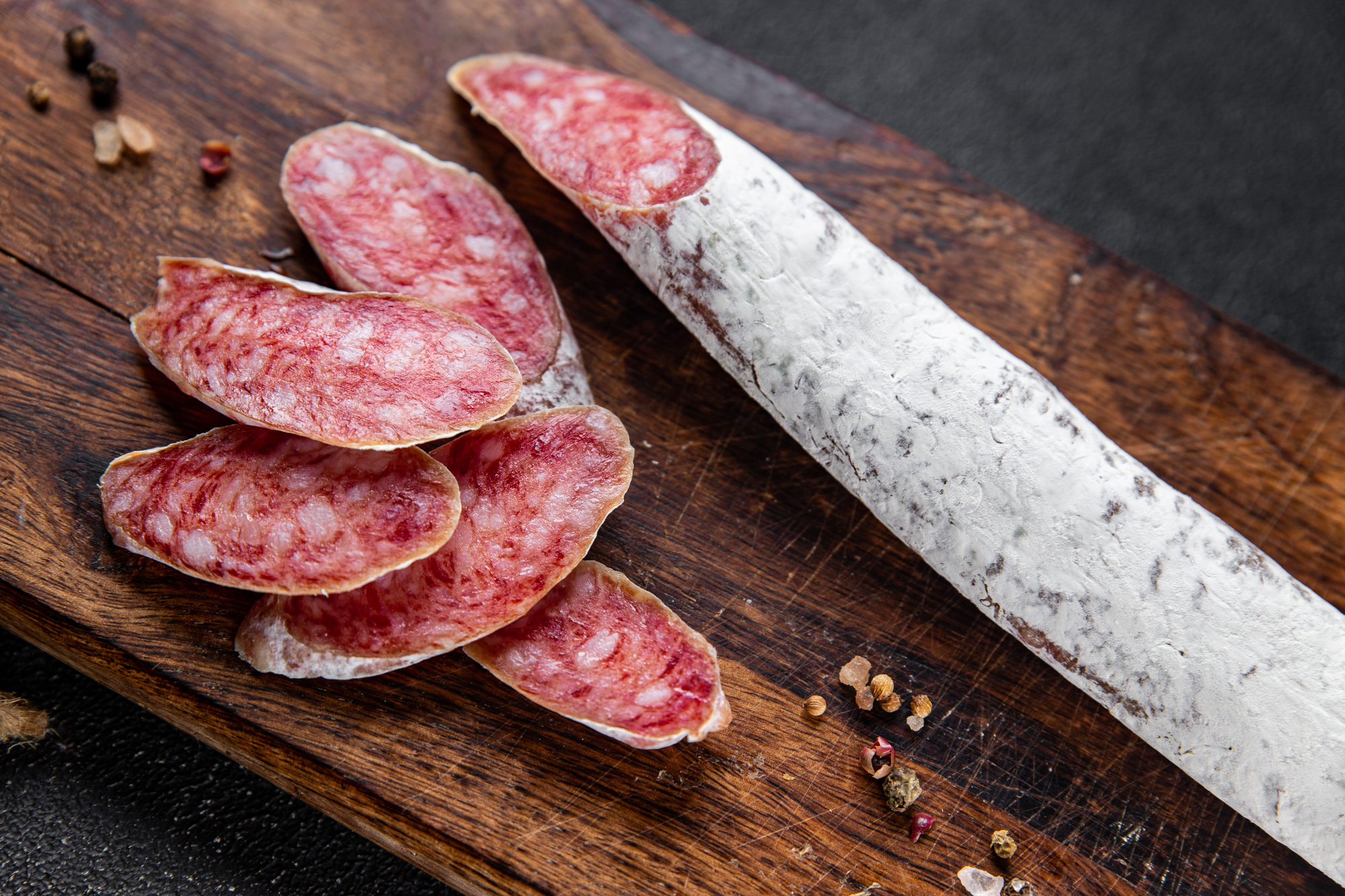 Salsiccia o salame intero e affettato su un tagliere di legno