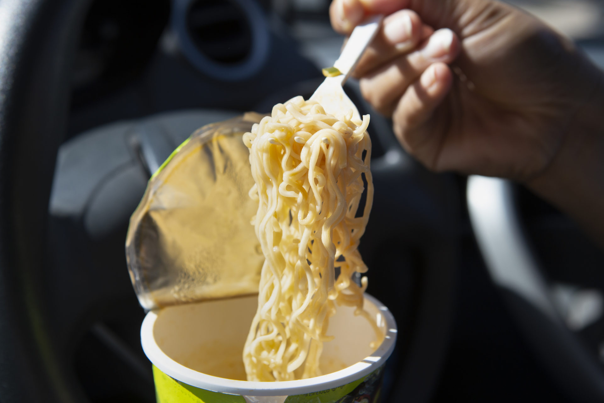 Impiegato che mangia noodles in auto durante l'ingorgo.