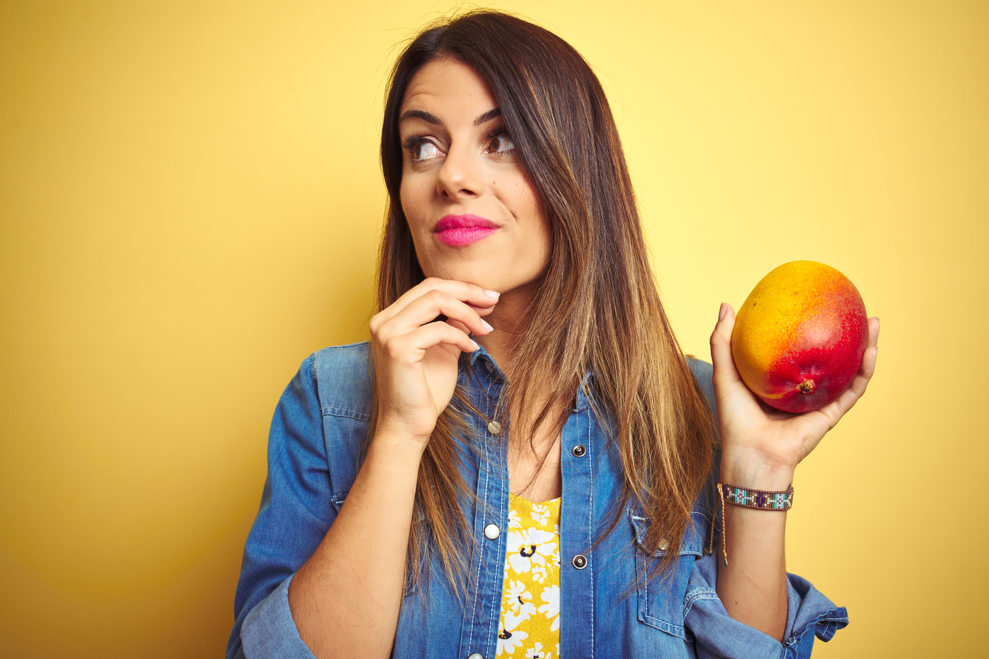 Giovane bella donna che mangia mango fresco e sano su sfondo giallo viso serio pensando alla domanda, idea molto confusa