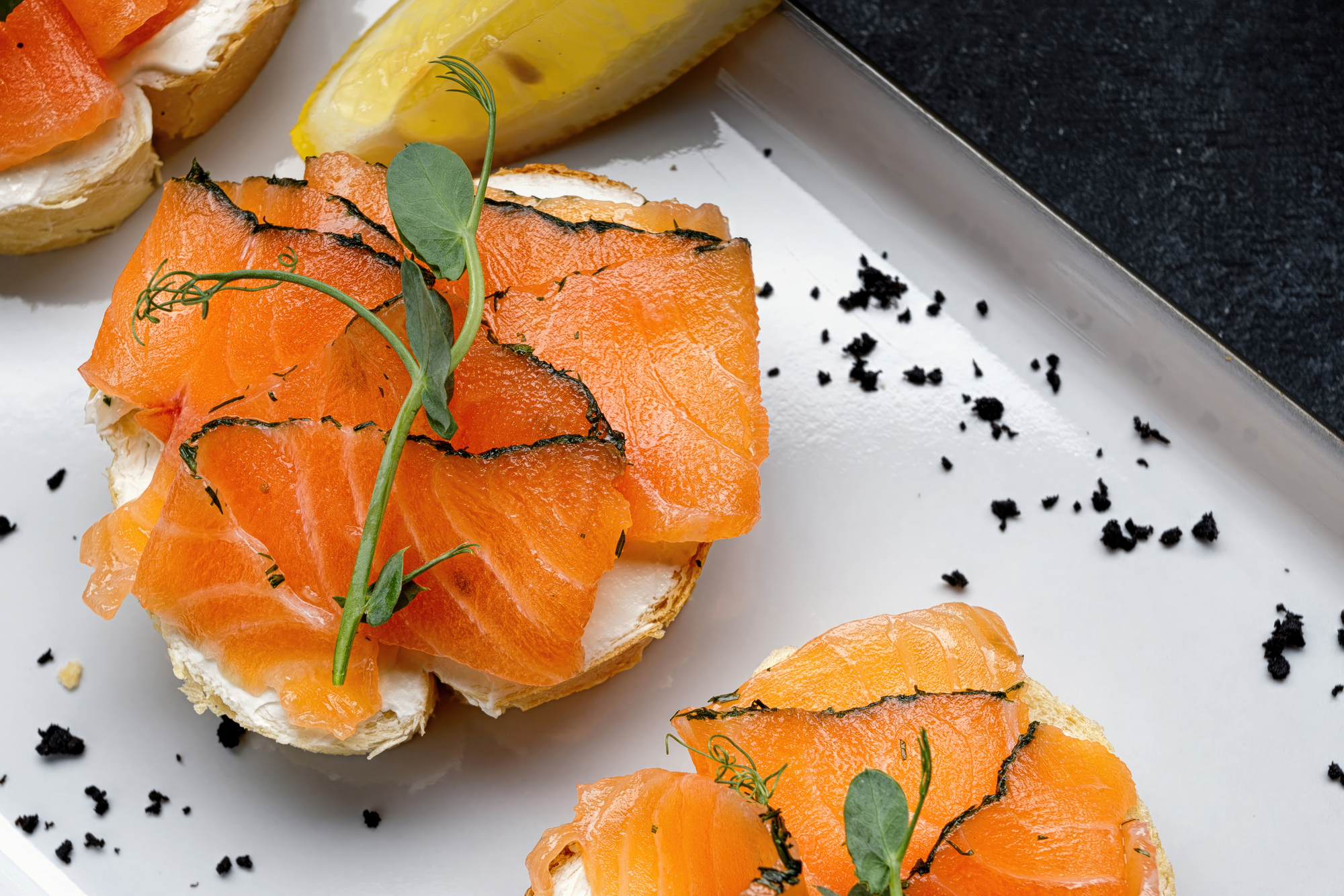 Bruschette con salmone affumicato, burro, erbe e pepe su un vassoio con fetta di limone