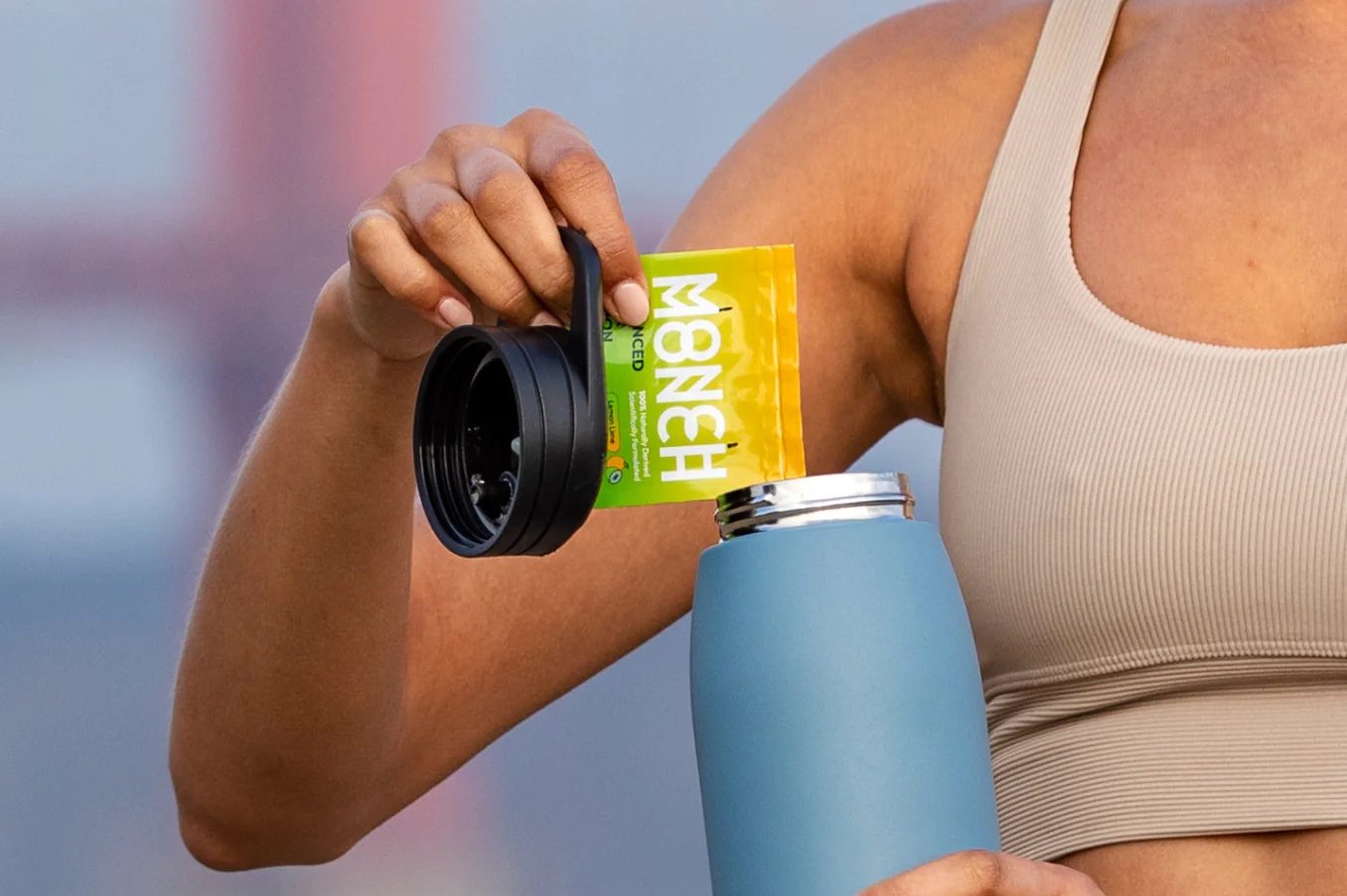 Donna in tenuta sportiva versa bustina di integratore Monch Monch in una borraccia