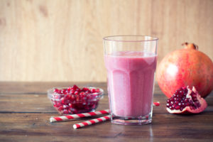 Bicchiere di frullato al melograno, con due cannucce, un melograno e una ciotola di semi rossi