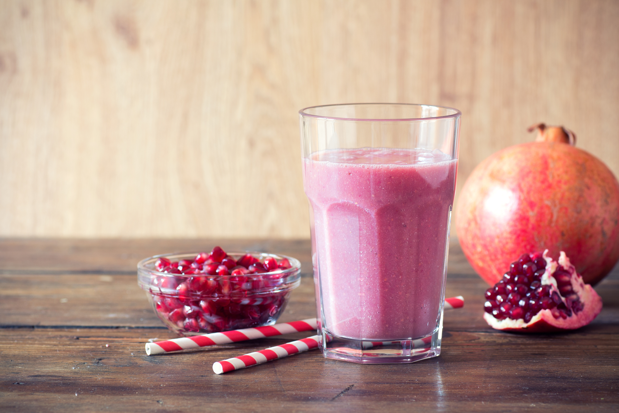 Bicchiere di frullato al melograno, con due cannucce, un melograno e una ciotola di semi rossi